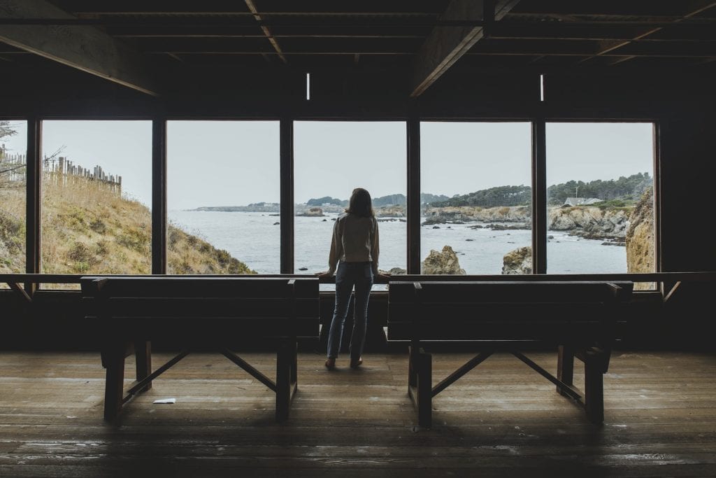 a woman looking at the ocean from inside a wooden building