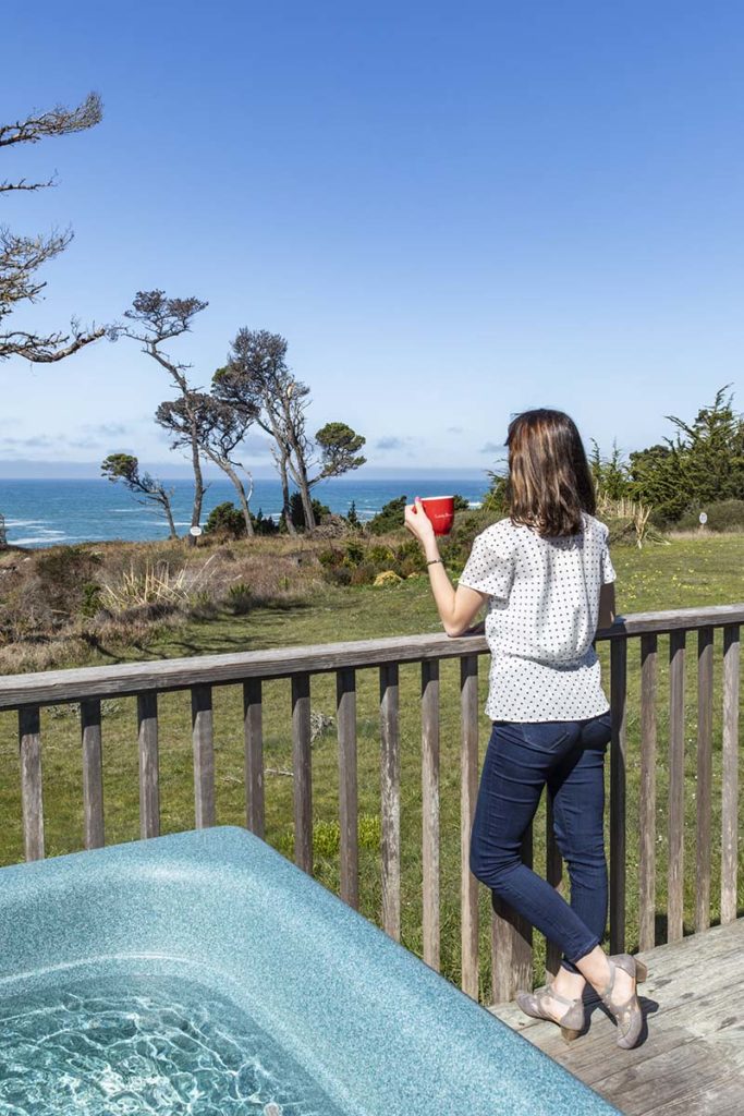 Woman standing next to hot tub looking over ocean near Mendocino in hotel room